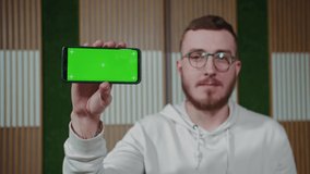 The guy shows the phone in a horizontal position with green screen chroma key background