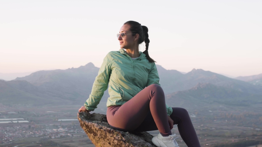 Hiker girl resting on a rock pedestal after long day trekking. Woman enjoying the sunset in nature.