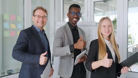 Positive colleagues business partners, diverse team, startup group project. African black man and caucasian man and woman show thumbs up and smile. Ethnic gender diversity, office workers
