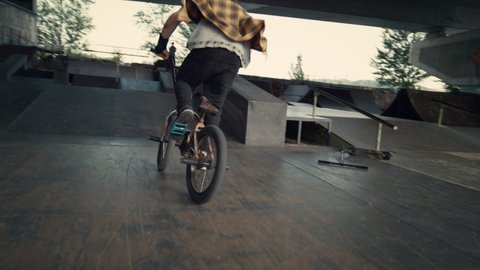 Active bmx rider performing tricks during freestyle session at skate park. Young male hipster jumping with bmx bike at city skatepark. Extreme biker having fun with bicycle outdoors. Leisure concept.
