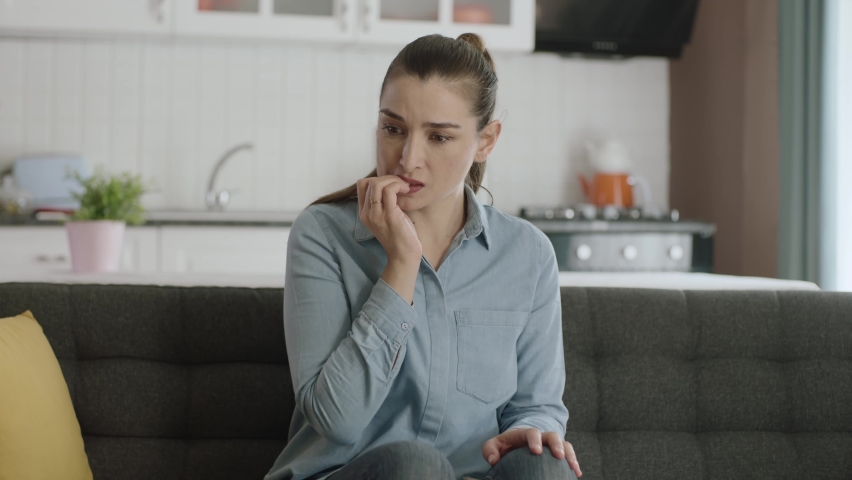 Nervous woman feeling panic, biting her nails, feeling anxious and confused. Frustrated and stressed woman waiting for someone at home. Angry woman biting her nails. Feelings of anxiety, fear. | Shutterstock HD Video #1089996735