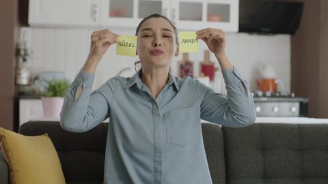 Video of happy woman dancing holding paper notes with "beautiful mommy" in Turkish over her eyes. Valentine's Day, mother's day, father's day, romantic concept.