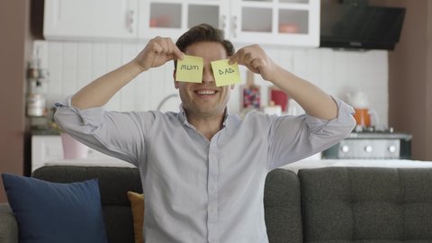 Video of happy man dancing holding paper notes with mom and dad over his eyes.Man dancing on the sofa of his house with papers in his eyes.Valentine's day, mother's day, father's day,romantic concept.