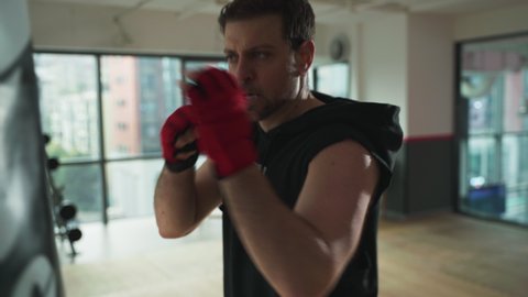 White man doing boxing in gym, feverishly hitting the sandbag heavily, doing exercise excitedly, hitting and kicking