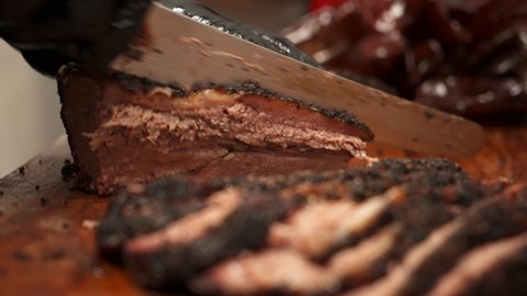 Pitmaster thinly slices Texas barbecue beef brisket in commercial restaurant kitchen, carving juicy lean moist traditional smoked brisket on cutting board, slow motion close up 4K