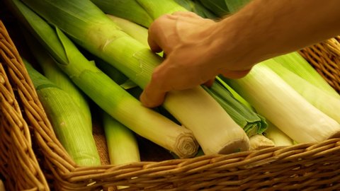 Close-up of many beautiful leeks in a wicker basket and a male hand takes one