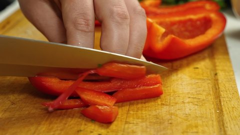 In the close-up, the cook is slicing red bell peppers on the cutting board. Vegetarian Cuisine. The concept of delicious and healthy food