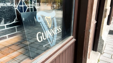 Strasbourg, France - Apr 10 2022: Guinness brewed in Dublin logotype on the showcase glass facade of pub bar with reflection of empty chairs in background