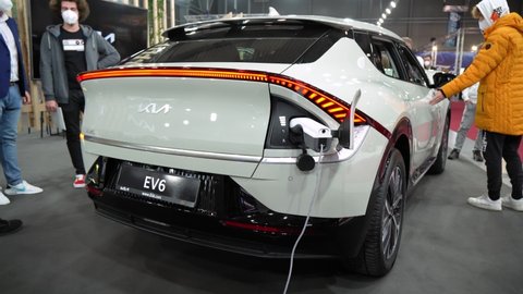 PRAGUE, CZECH REPUBLIC - NOVEMBER 14, 2021: White Kia EV6 charges on an EV charger at a car exhibition - rear view - people examine the car