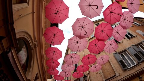 Grasse, France, October 3, 2021: SLOW MO Suspended pink umbrellas in the historic center of Grasse, celebrating the Rose Expo. Elements of architecture of Grasse with colored umbrellas between houses.