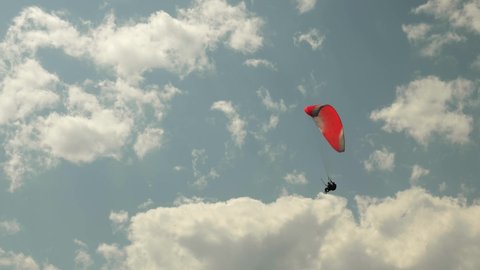 Paraglider flying with red parachute on background of sun and beautiful clouds. Paragliding in sky. Extreme sport concept. Person flying on paraglide over coastline at sunny summer day