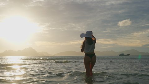Slow Motion Wide Handheld Shot Of Young Woman In Thong And Sun Hat Watching Glowing Sun Setting Over Sea From Corong Corong Beach, Philippines