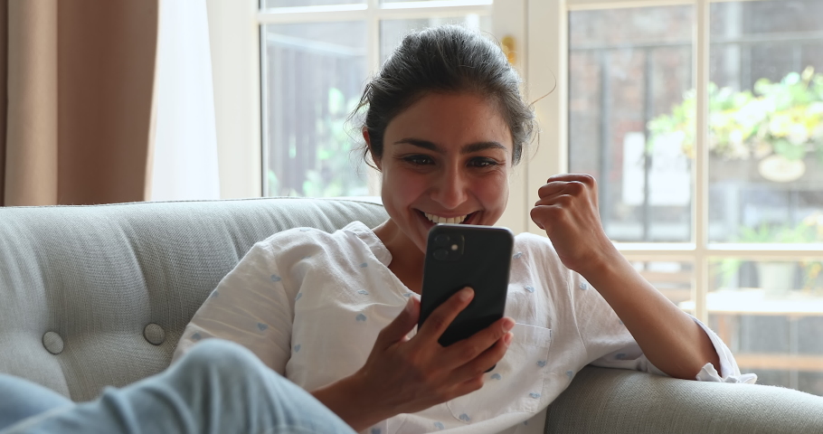 Excited overjoyed Indian female customer look on phone screen scream yes reading unbelievable news about seasonal sale at favorite web store. Euphoric young lady achieve success winning online lottery