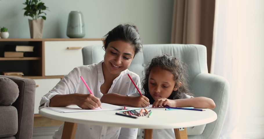 Happy Indian mom nanny help little girl to draw colorful picture in album using bright colored pencil kit. Young mother daughter kid having warm relationship relax on weekend enjoy coloring sketches Royalty-Free Stock Footage #1090009007
