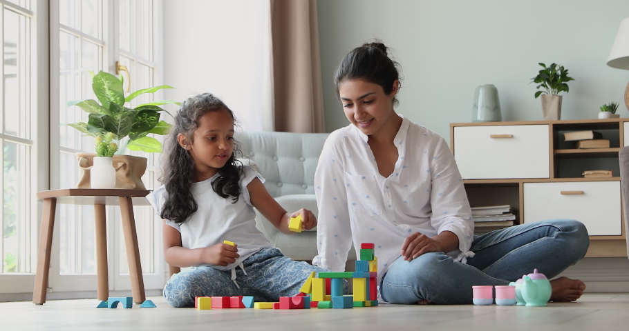 Smart little Indian girl play on warm floor with mom construct from brick set receive praise from parent. Happy preschooler child give high five to mum celebrate success in building fantasy toy castle Royalty-Free Stock Footage #1090009065