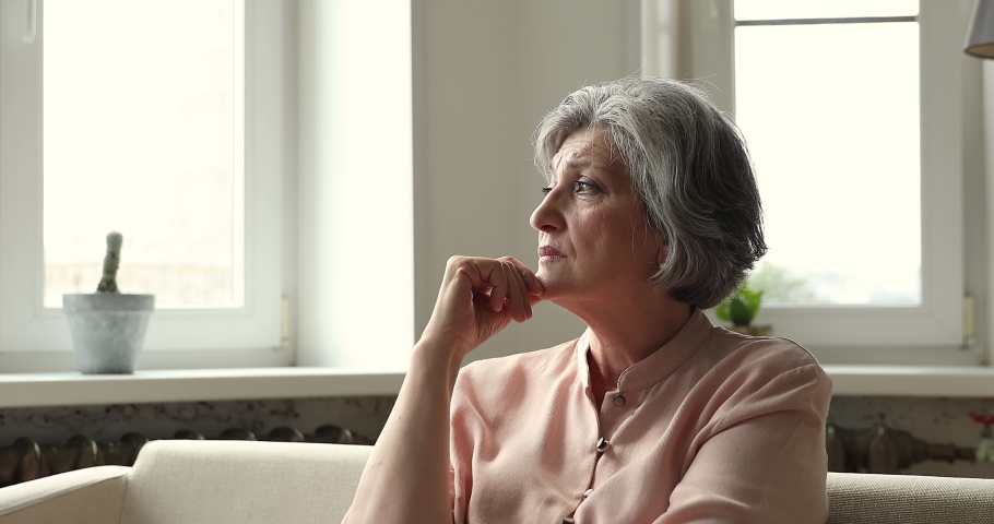 Sad unhappy elderly Latin lady retiree sit on couch alone rub chin hold back tears suffer of loneliness depression older age crisis. Upset stressed mature female grandma grieving feeling bad abandoned | Shutterstock HD Video #1090009097