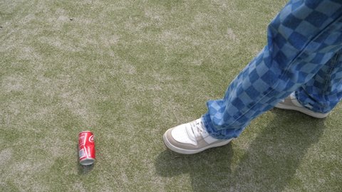 WROCLAW, POLAND - MAY 06, 2022: Teenager boy legs walk kicking empty coca cola can over artificial surface of playground