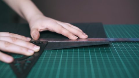CU: Professional designer measures black leather cloth with metal and plastic rulers on cutting board close view