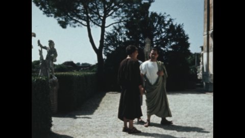 Decade 1950s: Roman villa exterior. Men talk on steps of Roman villa. Men in Roman age gardens. Man in toga. Stone statues in garden courtyard.