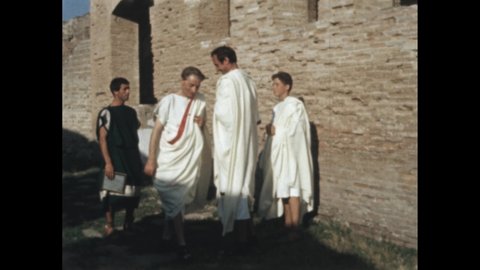 1950s 100 BC: Person crouches, picks grapes, sits with woman, children, they eat. Bowl on pedestal. Men wear togas, stand outside door. City, trolley passes, pedestrians walk.
