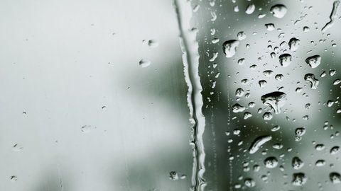 The car's wiper cleans the glass and creates movements of water shapes.macro water drops flowing on a window glass