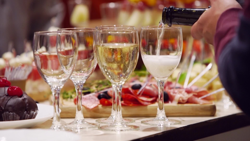 Waiter pouring glasses with champagne on catering service on banquet table with canape snacks in restaurant or hotel. Food set on birthday, wedding celebration or business conference event venue. | Shutterstock HD Video #1090016655