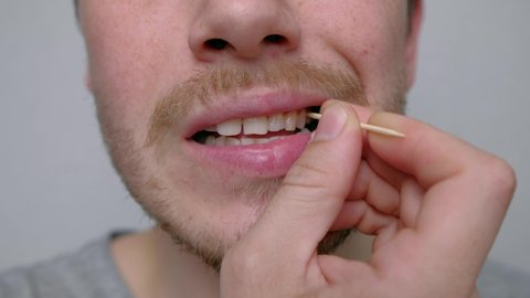 Using Toothpick. Etiquette and Good Manners. Close Up. A young man takes out the remnants of food stuck in his teeth with a toothpick close-up 