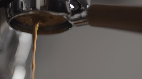 Slow motion low angle bad shot of espresso extraction from naked portafilter into white cup