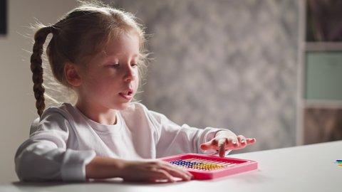 Inspired little blonde girl learns to count with colorful traditional toy abacus sitting at desk at mental arithmetics lesson closeup slow motion