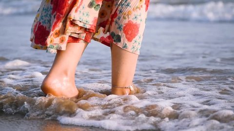 Close up shot of ocean waves washing over feet of young female. People enjoying summer vacation at tropical beach. Girl standing on seashore and enjoying tides of sea on trip
