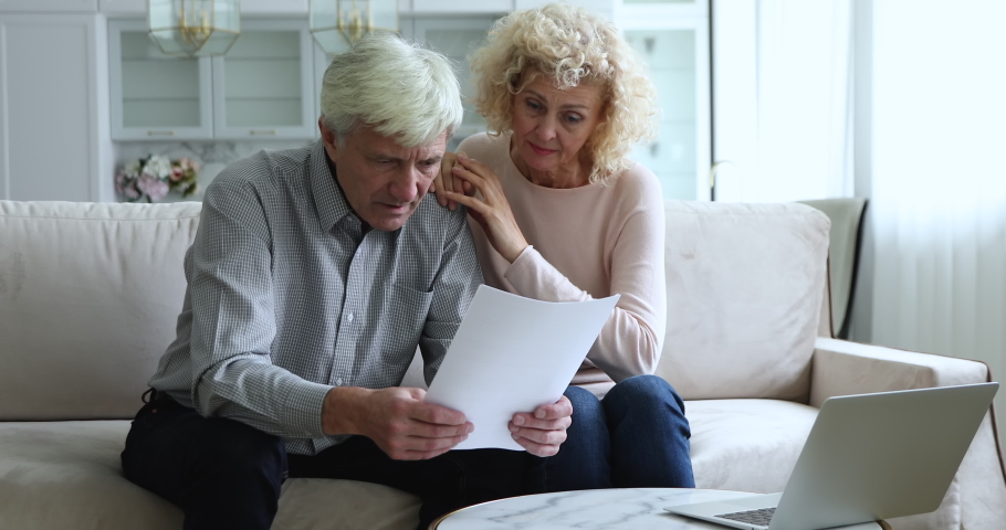 Mature couple sit on sofa read received paper notification feel stressed looking desperate, bank debtor spouses get legal reasons for eviction, non-payment of rent, bankruptcy, bad news from relatives | Shutterstock HD Video #1090023173