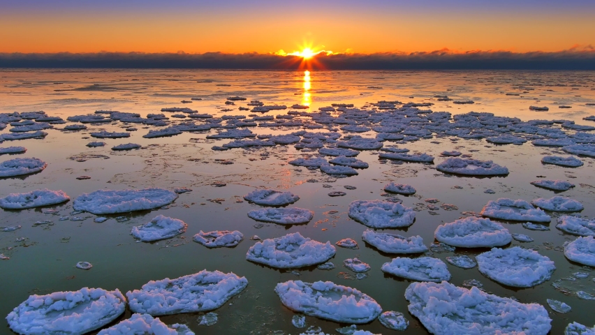 Bright stunning sunrise breaks over fog bank on a desolate subzero Lake Michigan, as the surface begins to freeze and ice-up. Aerial view. Royalty-Free Stock Footage #1090023347
