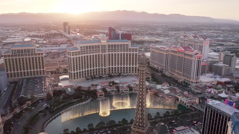 Golden sunset view above Las Vegas cityscape with cinematic mountains view. Impressive Bellagio fountains show illuminated in dusk under pink sky over horizon. Las Vegas Strip Nevada, USA April 2022
