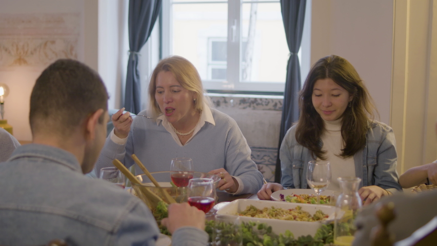 Happy Caucasian family enjoying dinner together at home while having family celebration party. Beautiful blonde woman and her daughter passing plate for putting food on it. Family, dinner concept