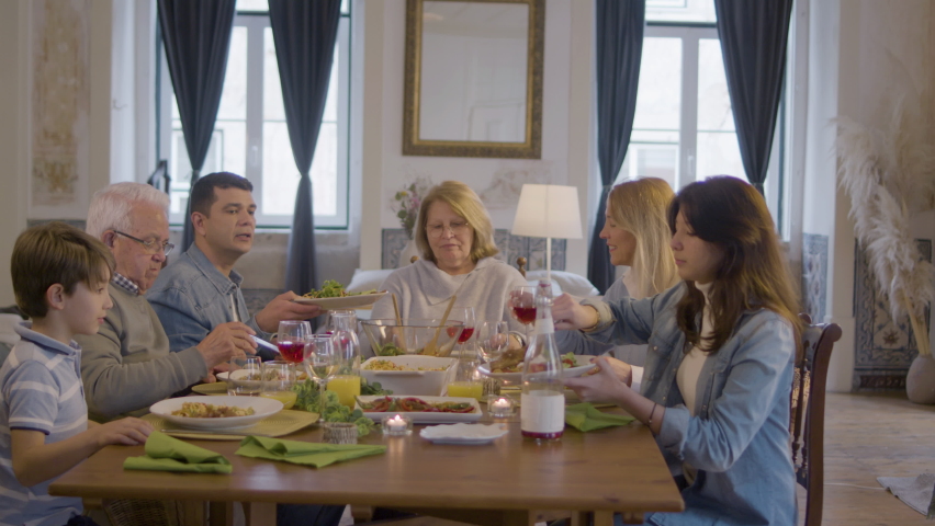 Happy Caucasian family enjoying dinner together at home while having family celebration party. Grandmother sitting at top of table, then everyone turning to camera and smiling. Family, dinner concept