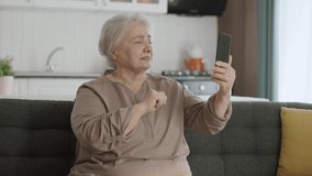 Happy old grandmother holding mobile phone, making video call with loved ones, happy old grandmother waving. Elderly woman learning to use modern technology device. Technology use in the elderly.