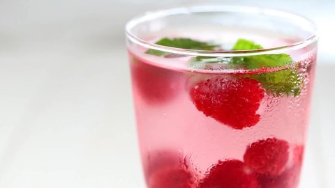 Raspberry cocktail.Splashes and drops of a Summer drink. glass with raspberry pink drink.raspberries in a glass with water, berries and raspberry leaves on a white wooden table. 