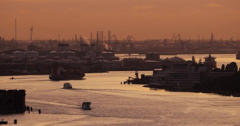 Cargo ship traffic through the ports of Rotterdam, busiest industrial port of Europe. Container ship in twilight, oil storage silos in the background