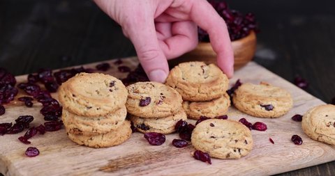 to put oatmeal cookies with dried cranberries on the board, a person puts cookies with red cranberries on the board with his hand