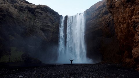 Man walking and standing near the Icelandic waterfall Skogafoss in Iceland, near the Skogar, slow-motion background wallpapers. Beautiful landscape. High quality 4k footage. Wide angle shot
