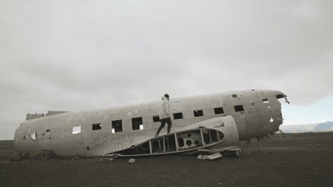 Man in white lonely sad walking on old crashed broken wreck Icelandic plain dc-3 landmark in Iceland. High quality 4k footage in slow motion. Apocalyptic catastrophe lost view