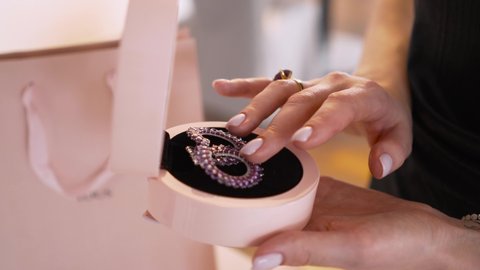 The woman is touching her expensive luxury earrings in a box as a gift from her boyrfriend, close-up view.