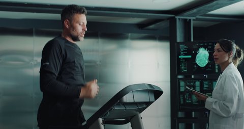 Cinematic shot of athlete is doing cardio workout for endurance test of body resistance by training on treadmill while physician monitoring heart rate, pulse and ECG data in modern medical laboratory.