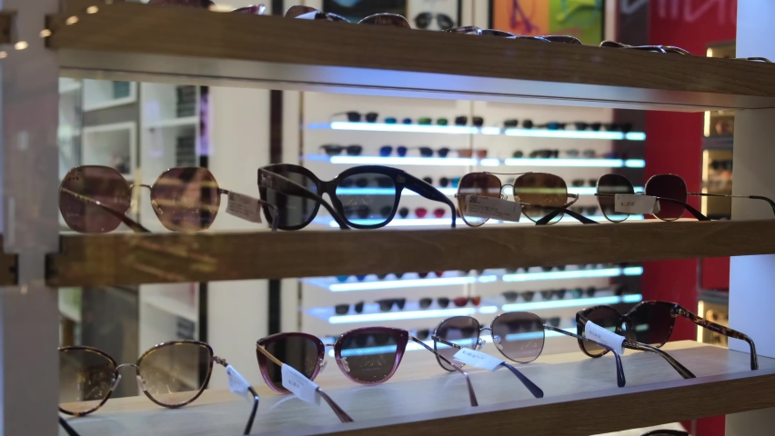 Optics shop. The windscreen offers a wide selection of sunglasses. From glasses with brown, gray and green lenses to red in a fashionable, light frame and different materials. Royalty-Free Stock Footage #1090036667