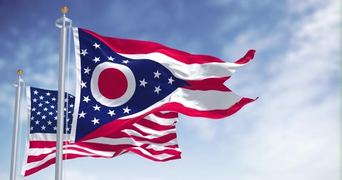 The Ohio state flag waving along with the national flag of the United States of America. In the background there is a clear sky. Ohio is a state in the Midwestern region of the United States