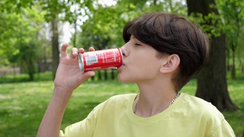 WROCLAW, POLAND - MAY 06, 2022: Portrait of cute young teenager kid boy drinking coca cola red can sweet carbonated beverage