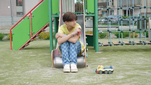 WROCLAW, POLAND - MAY 06, 2022: Lonely sad teenager kid boy drinking coca cola can sit on a slide of playground for children