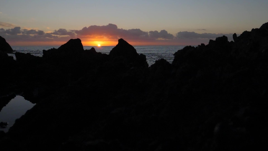 Ocean side sunrise as the sun appears through the jagged rocks silhouette. Tracking so the sun appears or disappears.  | Shutterstock HD Video #1090043279