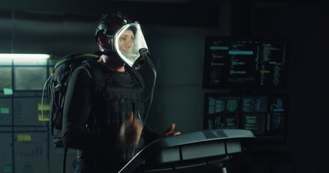 Science fiction shot of futuristic astronaut with oxygen visor mask and weight vest is doing workout for endurance test of body resistance by training on treadmill in modern medical laboratory.