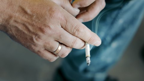 Man holding a smoking cigarette in his hand close up. Bad lifestyle and bad habits. Smoking cigarette in the smoker's hand.